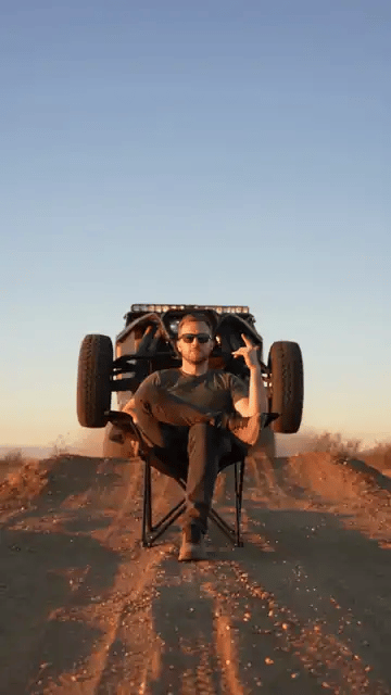 The human car jump AI video: a man in sunglasses gestures from his chair as the racing truck launches off the mound and over his head