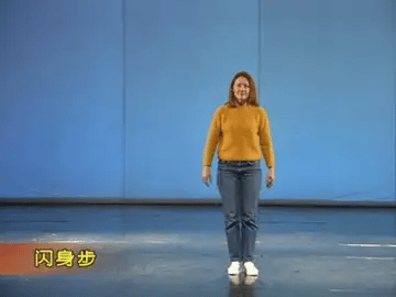 A woman in a mustard sweater and jeans dodges and lunges in the blue studio