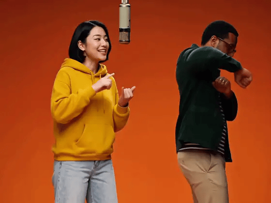 AI-generated Hotel Lobby example: two people in a yellow hoodie and a dark green jacket performing in front of an orange wall