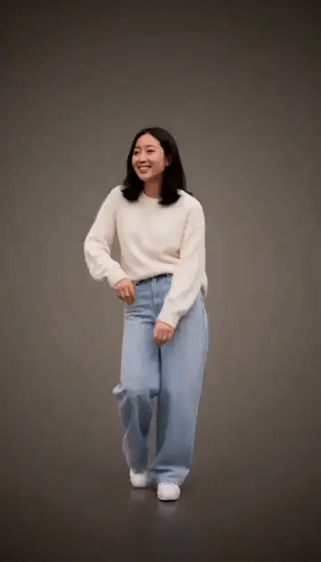 A woman in a cream sweater and wide-leg jeans does the opening steps of the Jean Phil dance in a grey studio