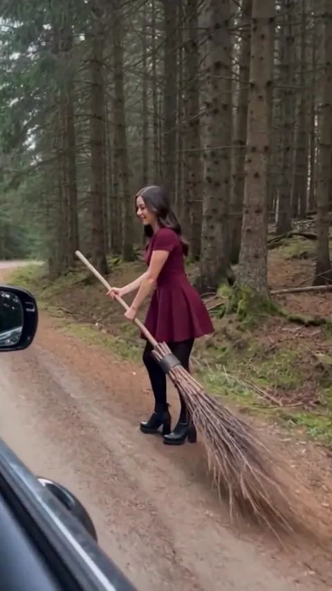 Die Person auf dem Besen schaut in die Kamera, während sie neben dem Auto hergeht